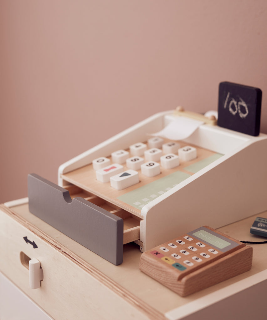 Kid's Concept  Wooden cash register in light colours. Perfect for the little kiosk or store. The cash register has buttons to press, a board to writh the prices on, includes a white chalk and compartments for bills and coins, and a card reader with two cards.  Age: 3y+  Size: 20 x 16.5 x 10cm