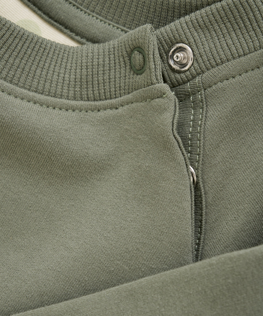 Details:  This baby sweatshirt in sea spray is the perfect addition to your child's wardrobe. With a round neckline, ribbed arm cuffs and waistband, and a cute turtle print on the front, it's both stylish and functional. Plus, the push buttons on the side of the collar make dressing your little one a breeze.   Color: Sea spray  Composition: Organic Sweat 95% Cotton/ 5% Elastane 