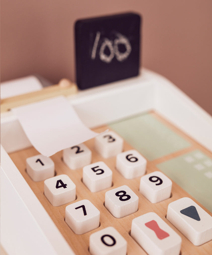 Kid's Concept  Wooden cash register in light colours. Perfect for the little kiosk or store. The cash register has buttons to press, a board to writh the prices on, includes a white chalk and compartments for bills and coins, and a card reader with two cards.  Age: 3y+  Size: 20 x 16.5 x 10cm