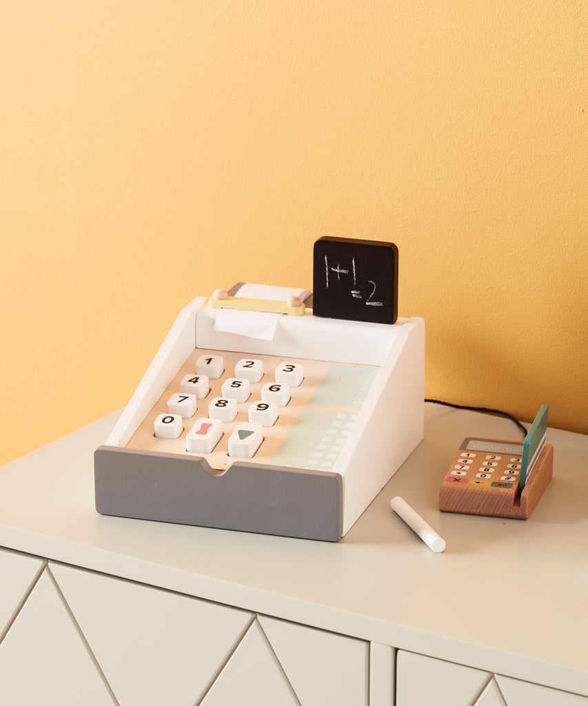 Kid's Concept  Wooden cash register in light colours. Perfect for the little kiosk or store. The cash register has buttons to press, a board to writh the prices on, includes a white chalk and compartments for bills and coins, and a card reader with two cards.  Age: 3y+  Size: 20 x 16.5 x 10cm