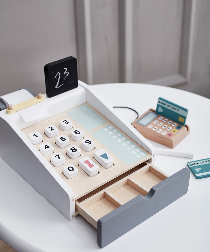 Kid's Concept  Wooden cash register in light colours. Perfect for the little kiosk or store. The cash register has buttons to press, a board to writh the prices on, includes a white chalk and compartments for bills and coins, and a card reader with two cards.  Age: 3y+  Size: 20 x 16.5 x 10cm