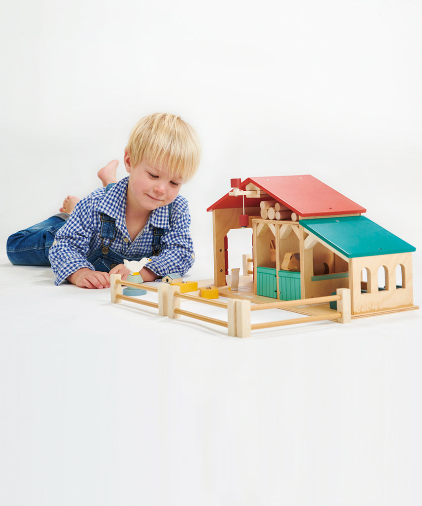 Tender Leaf®  Made throughout from top quality plywood, this farm has been designed to be open and accessible for little hands. It features a barn with barn doors and a feeding trough, 2 stables with opening doors, a ladder leading to hay loft, a pulley system with a magnetic end to lift the hay bales, a cowshed with feeding compartments, four fences, a stile, three hay bales, 2 geese, 2 horses, a grain trough, an animal feeding trough, a beehive and 6 logs. 