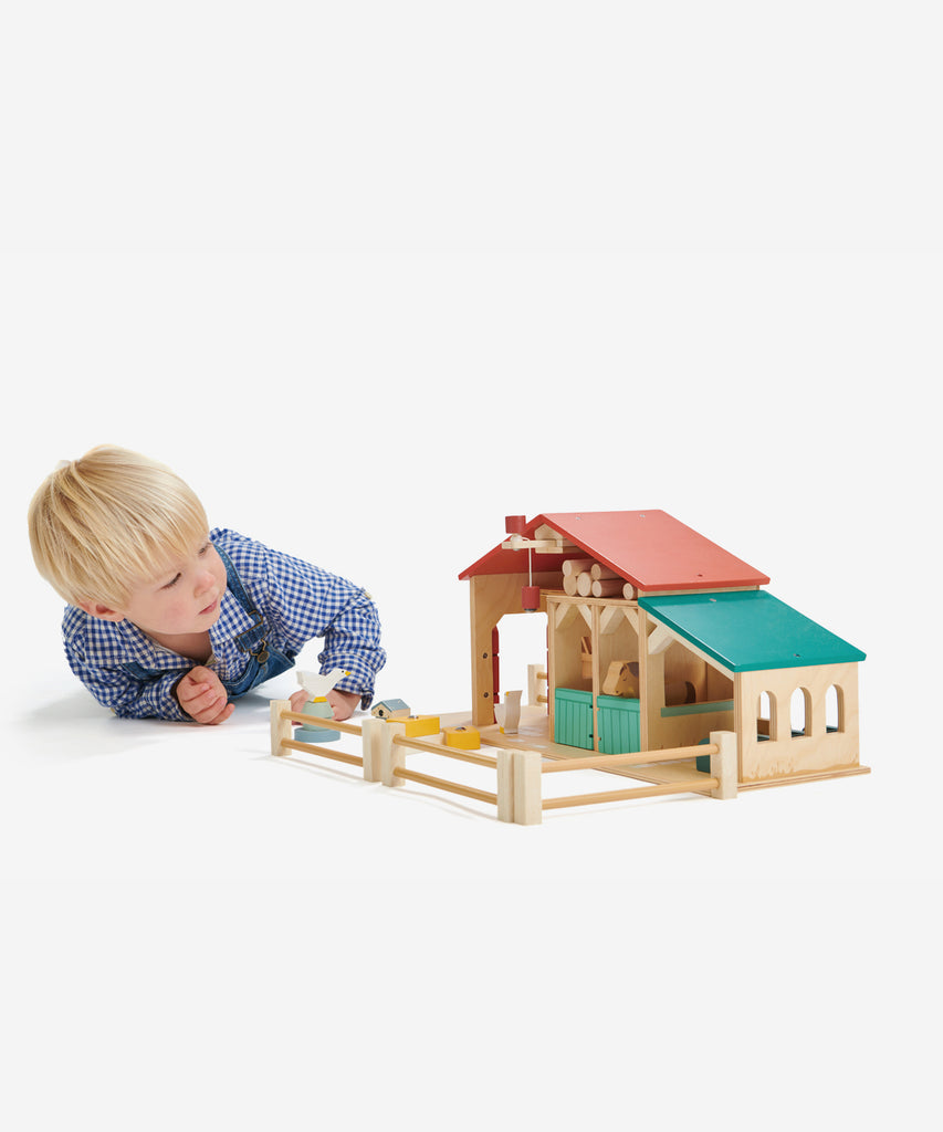 Tender Leaf®  Made throughout from top quality plywood, this farm has been designed to be open and accessible for little hands. It features a barn with barn doors and a feeding trough, 2 stables with opening doors, a ladder leading to hay loft, a pulley system with a magnetic end to lift the hay bales, a cowshed with feeding compartments, four fences, a stile, three hay bales, 2 geese, 2 horses, a grain trough, an animal feeding trough, a beehive and 6 logs. 