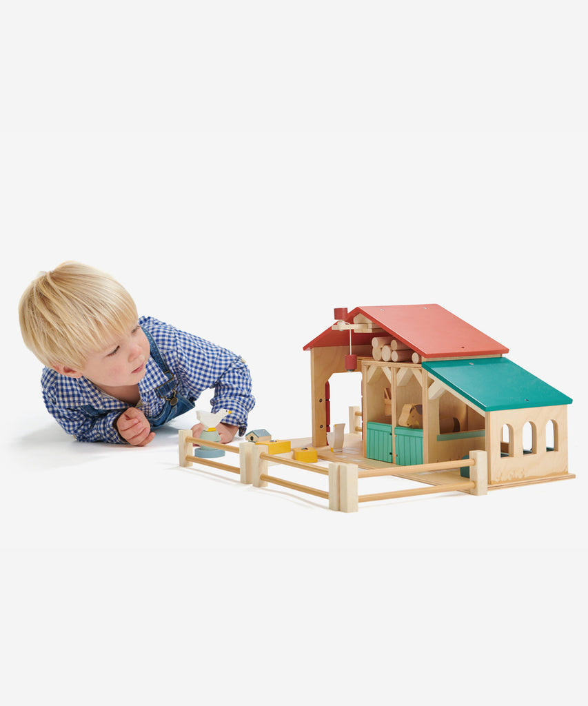 Tender Leaf®  Made throughout from top quality plywood, this farm has been designed to be open and accessible for little hands. It features a barn with barn doors and a feeding trough, 2 stables with opening doors, a ladder leading to hay loft, a pulley system with a magnetic end to lift the hay bales, a cowshed with feeding compartments, four fences, a stile, three hay bales, 2 geese, 2 horses, a grain trough, an animal feeding trough, a beehive and 6 logs. 